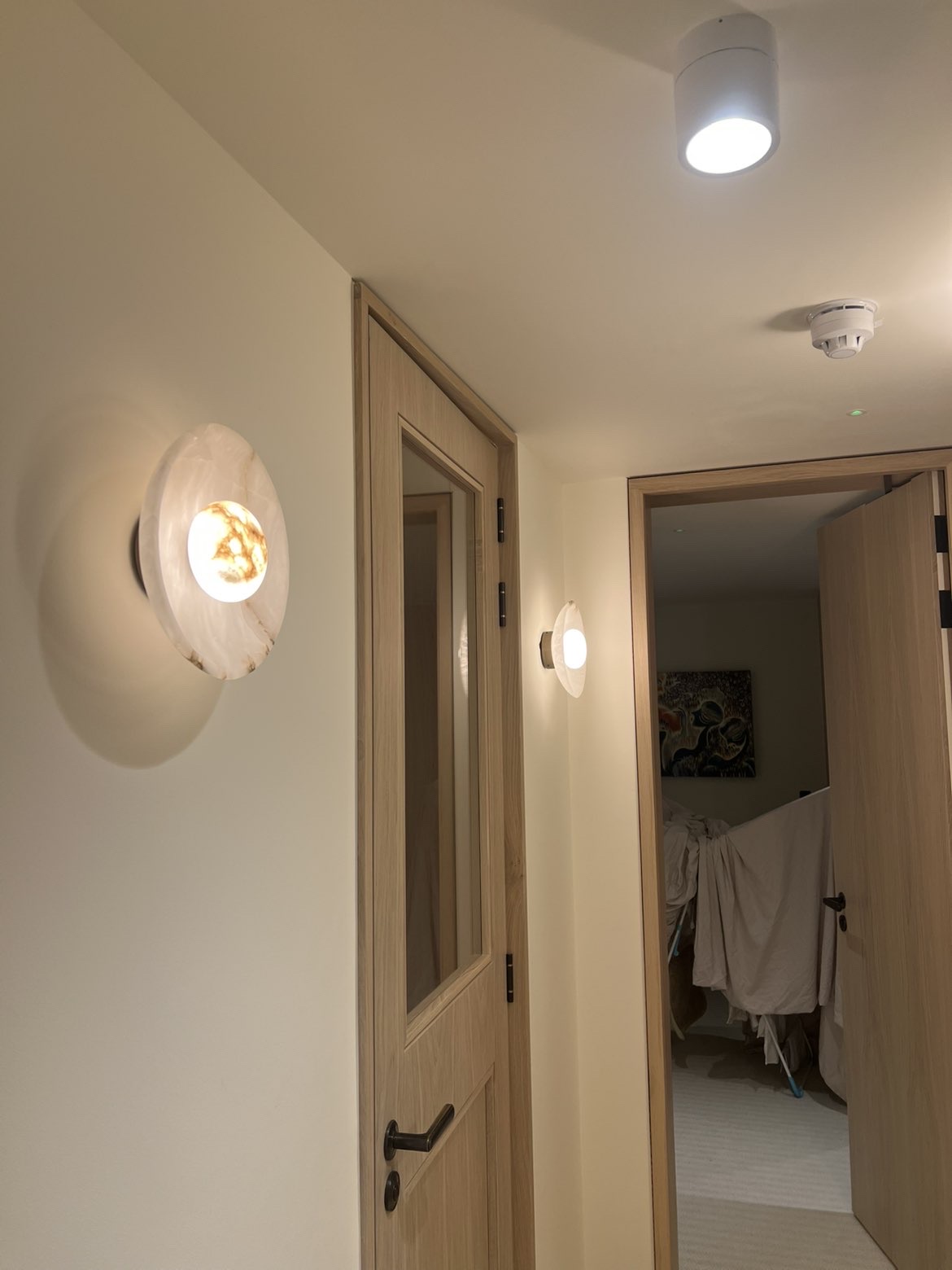 Two round alabaster wall lights lit in a hallway beside oak doors