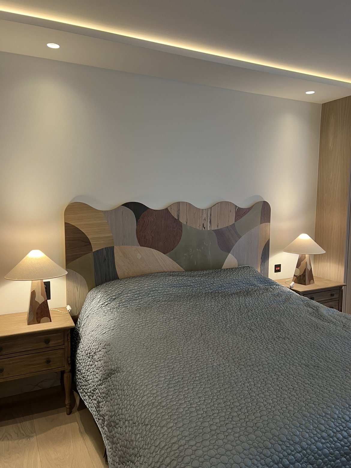 Bedroom with concealed cove LED strip lighting and recessed downlights above the bed
