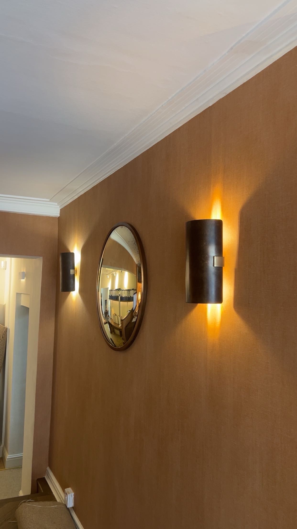 Two bronze wall sconces lit either side of a round mirror